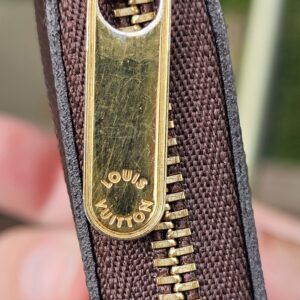 Gold-tone zip pull on the Louis Vuitton Monogram Giant Zippy Coin Purse held in hand