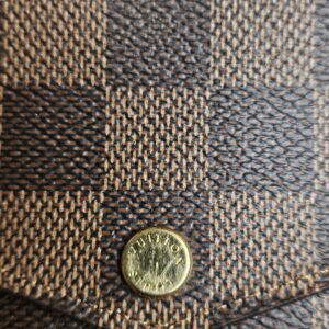 Close-up of the engraved gold-tone snap on the Damier Ebene flap