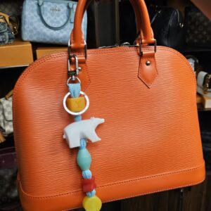 The charm clipped to an orange Epi handbag for styling. Only the charm is for sale