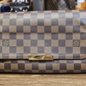 Front of the Damier Ebene Favorite MM with the gold-tone plate on the flap
