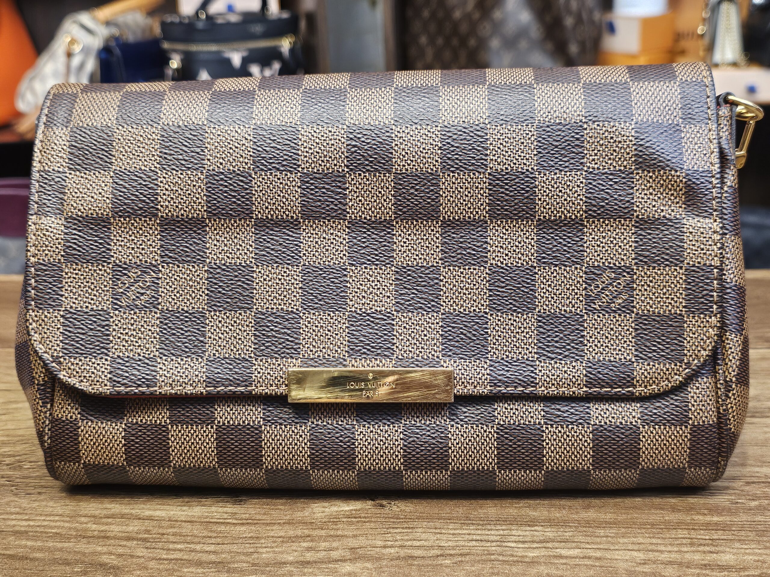 Front of the Damier Ebene Favorite MM with the gold-tone plate on the flap