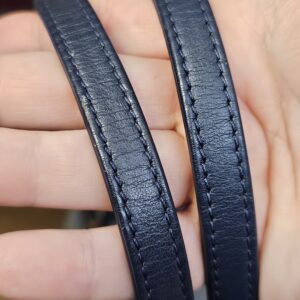Navy leather shoulder strap of the Deauville tote held in the hand