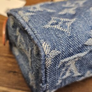 Base corner of the pouch showing the woven Monogram denim and yellow stitching