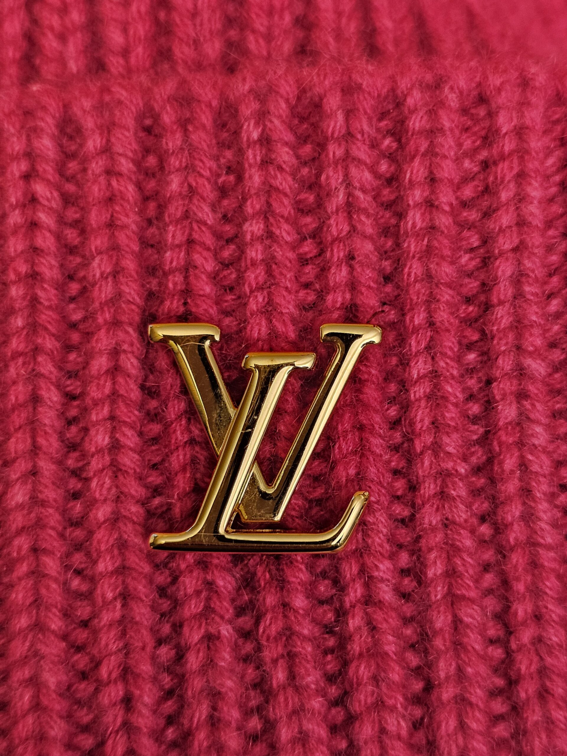 Close up of the gold tone LV logo on the fuchsia ribbed cashmere knit