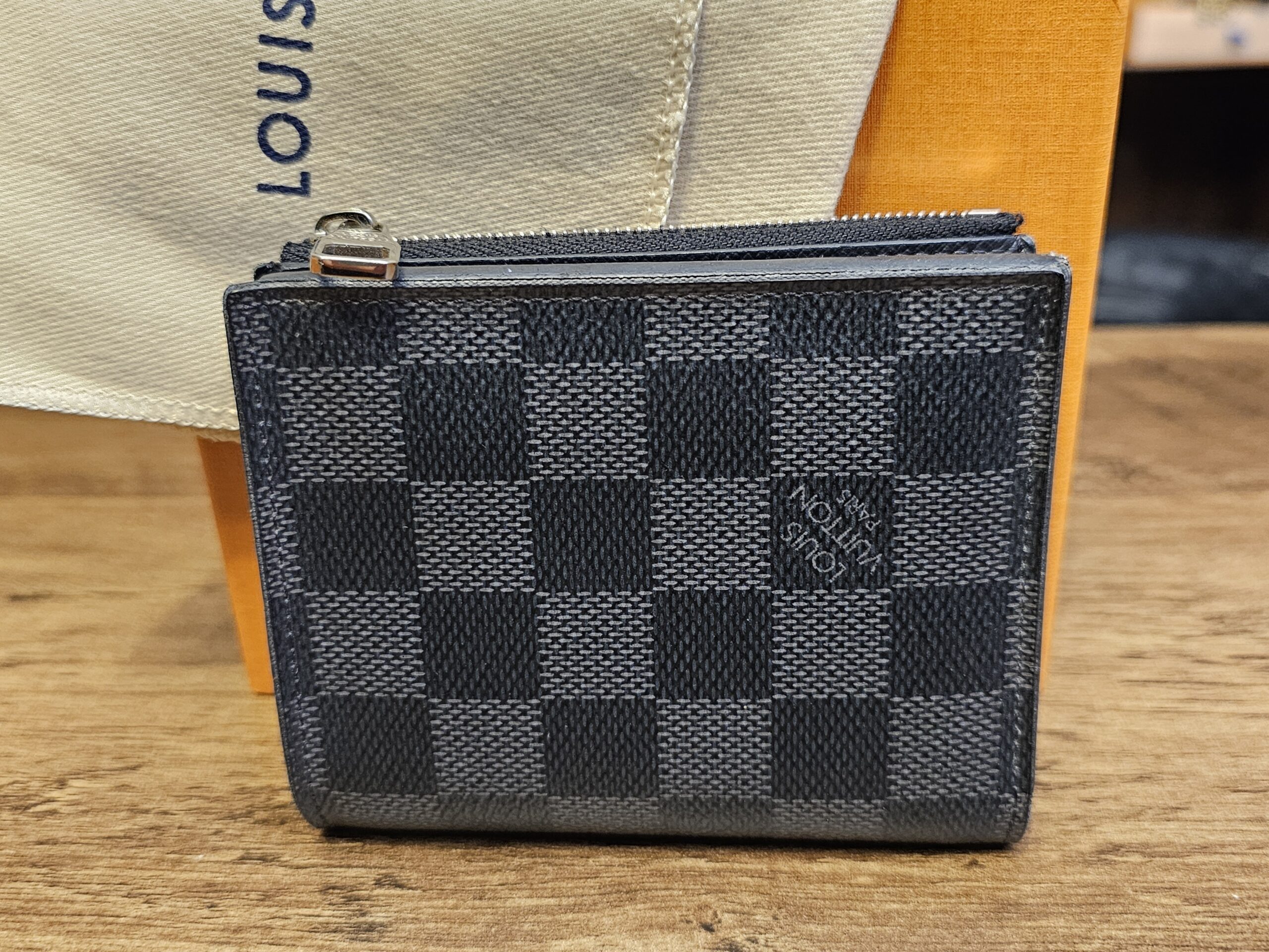 Louis Vuitton Damier Graphite Smart Wallet closed on its dust bag, showing the graphite check canvas and zip pull