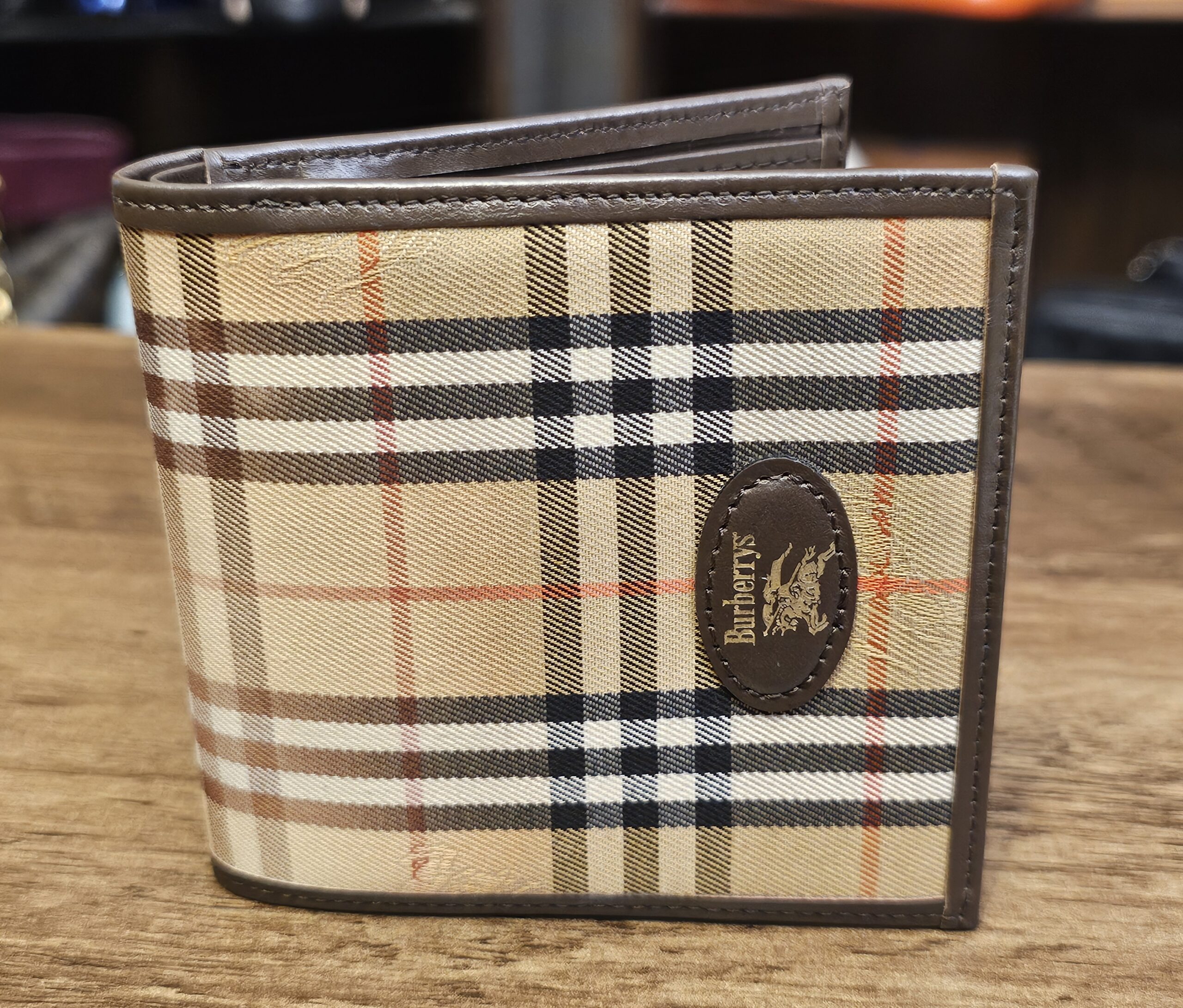 Burberrys Nova Check Bifold Wallet closed, showing the camel check canvas and the leather logo oval