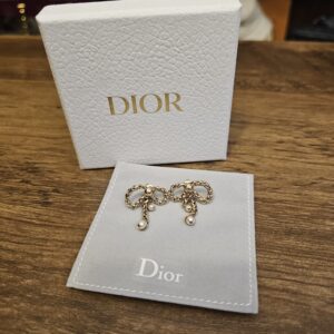 Dior box and pouch on a wood table with the gold-tone bow earrings resting on the pouch