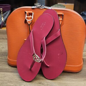 Sandal propped against an orange bag to show the berry color