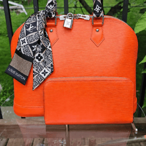 Bandeau tied on the handle of an orange Louis Vuitton Epi Alma outdoors