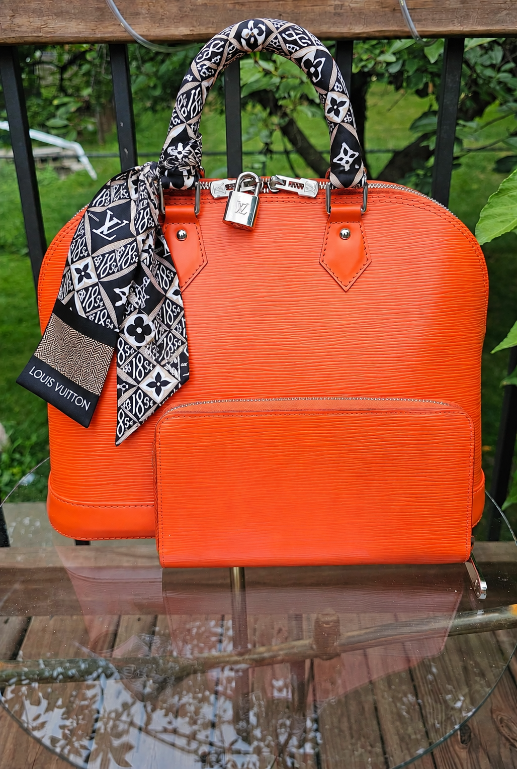 Bandeau tied on the handle of an orange Louis Vuitton Epi Alma outdoors