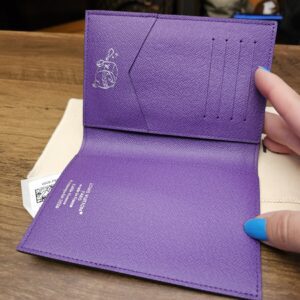 Open cover showing the purple leather interior, card slots and travel illustration